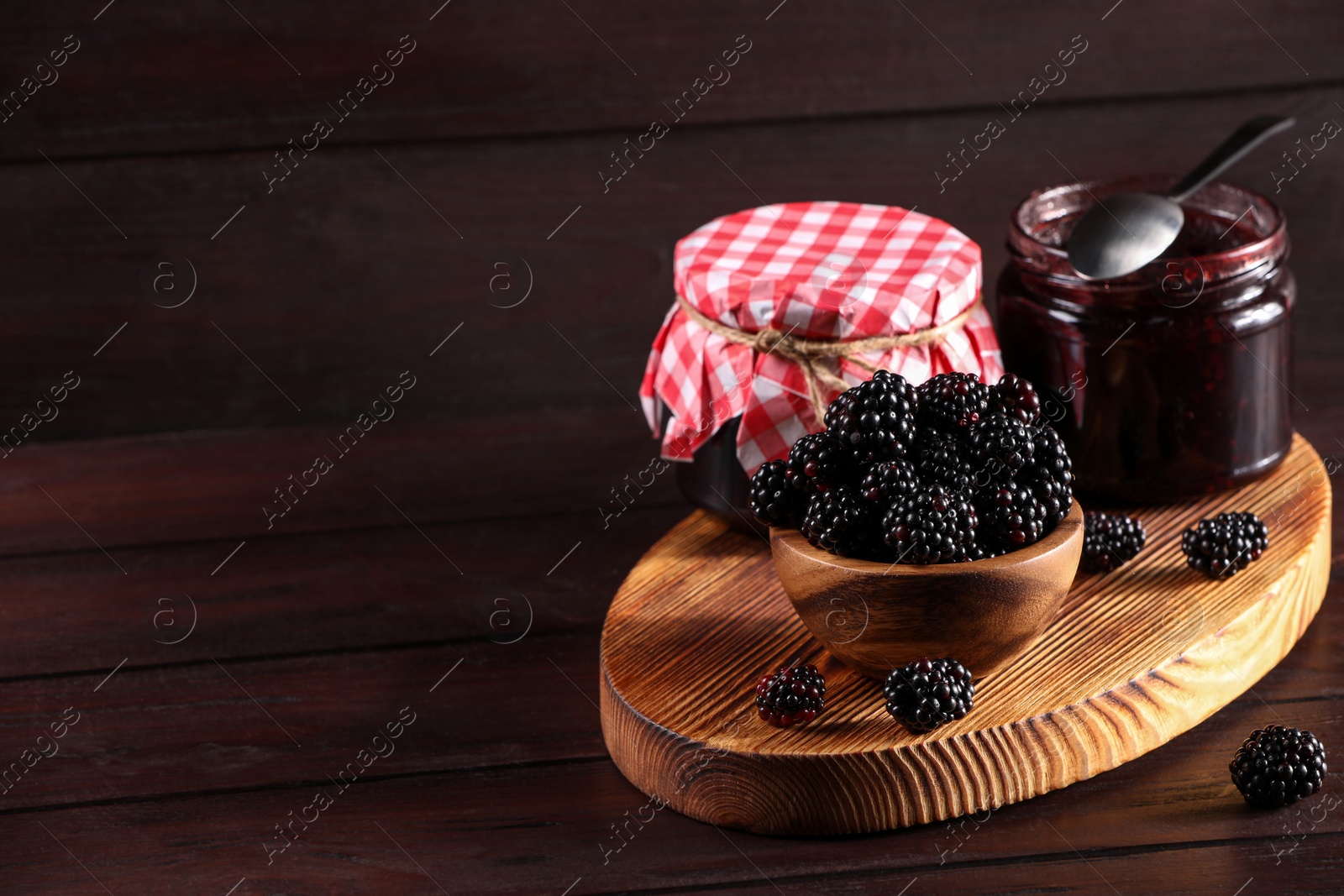 Photo of Fresh ripe blackberries and tasty jam on wooden table. Space for text