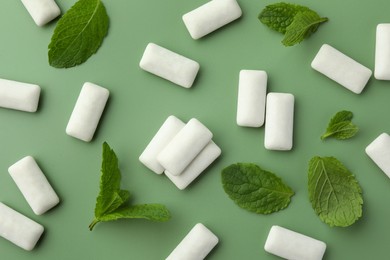 Photo of Tasty white chewing gums and mint leaves on light green background, flat lay