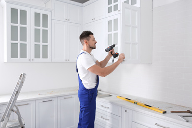 Photo of Worker installing handle on cabinet door with screw gun in kitchen