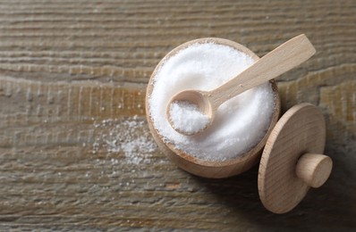 Photo of Organic salt in bowl and spoon on wooden table, top view. Space for text