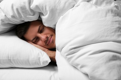 Handsome man sleeping under soft blanket in bed at home