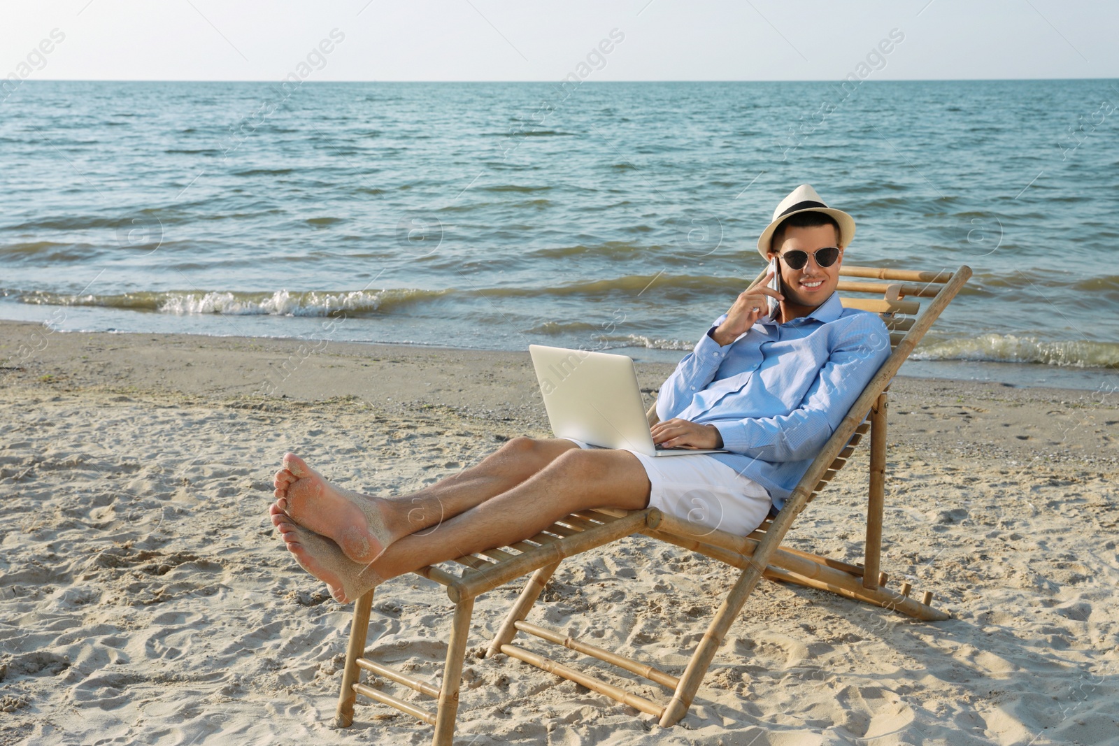 Photo of Happy man with laptop talking by mobile phone on beach. Business trip