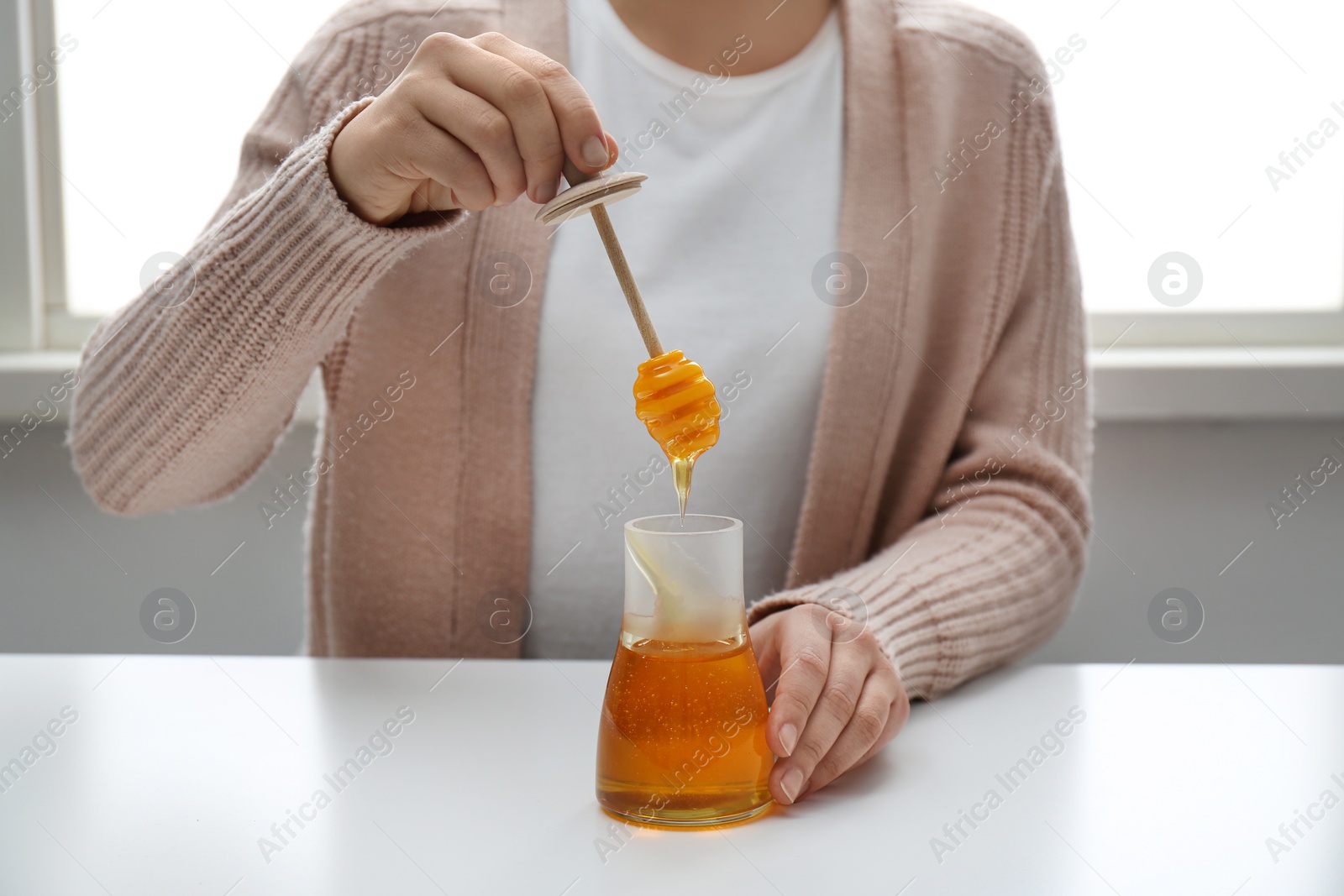 Photo of Woman with honey and dipper at white table, closeup