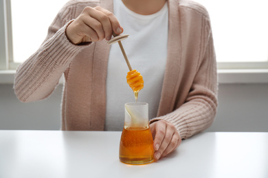 Photo of Woman with honey and dipper at white table, closeup