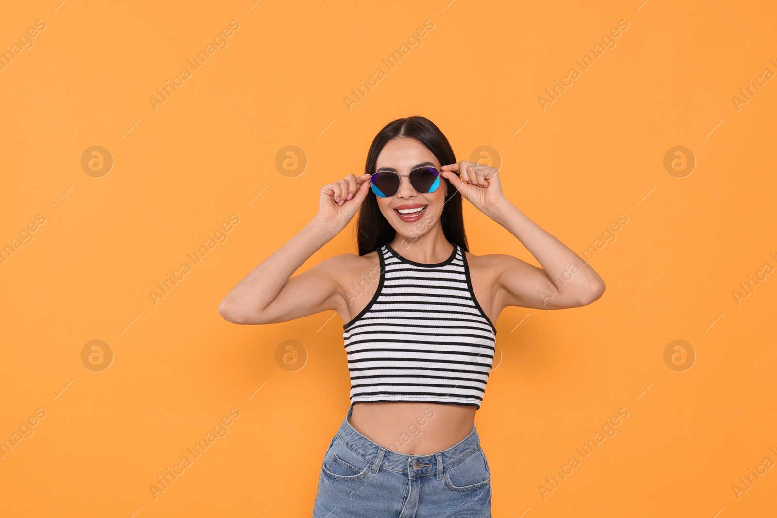 Photo of Attractive happy woman touching fashionable sunglasses against orange background