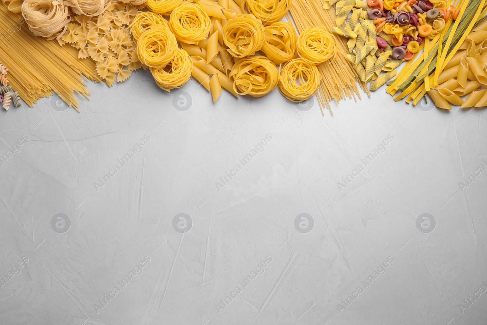 Photo of Different types of pasta on light grey table, flat lay. Space for text