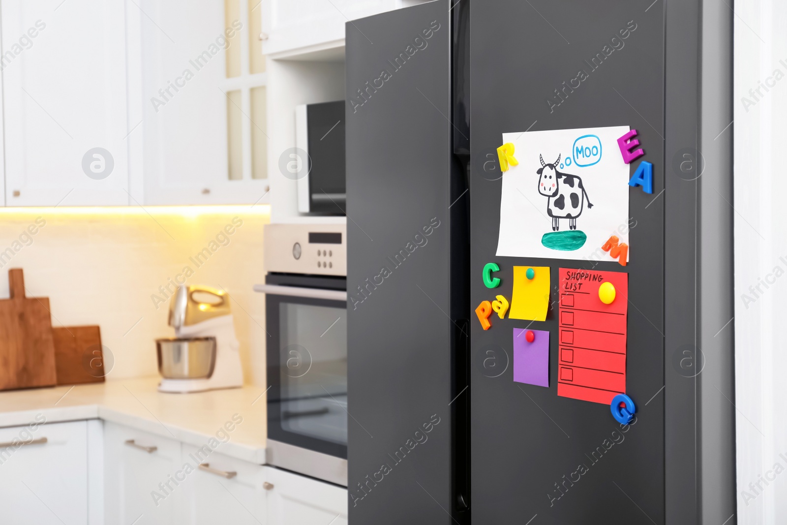 Photo of Modern refrigerator with child's drawing, notes and magnets in kitchen