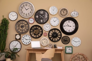 Stylish room interior with collection of wall clocks and workplace