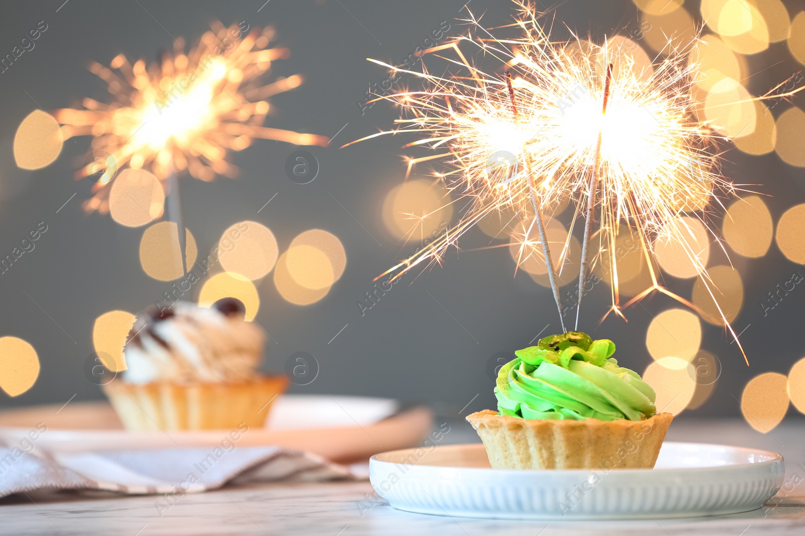 Photo of Cupcake with burning sparkler on table against blurred festive lights. Space for text