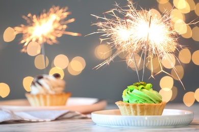 Cupcake with burning sparkler on table against blurred festive lights. Space for text