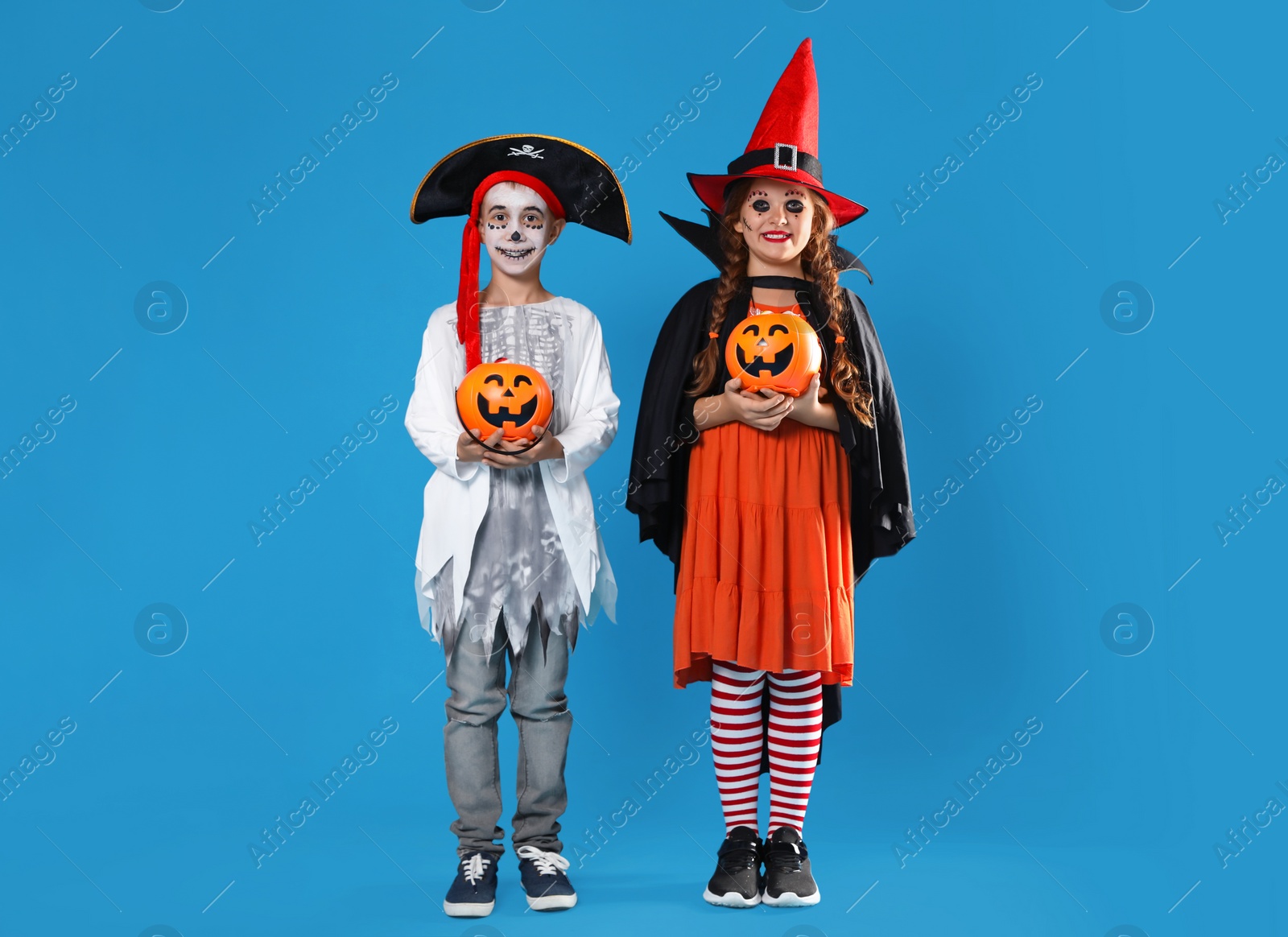 Photo of Cute little kids with pumpkin candy buckets wearing Halloween costumes on blue background