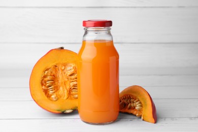 Photo of Tasty pumpkin juice in glass bottle and cut pumpkin on white wooden table