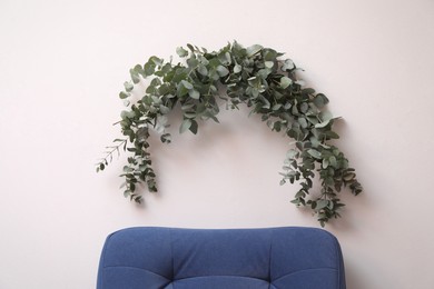 Beautiful garland made of eucalyptus branches hanging above armchair on white wall indoors