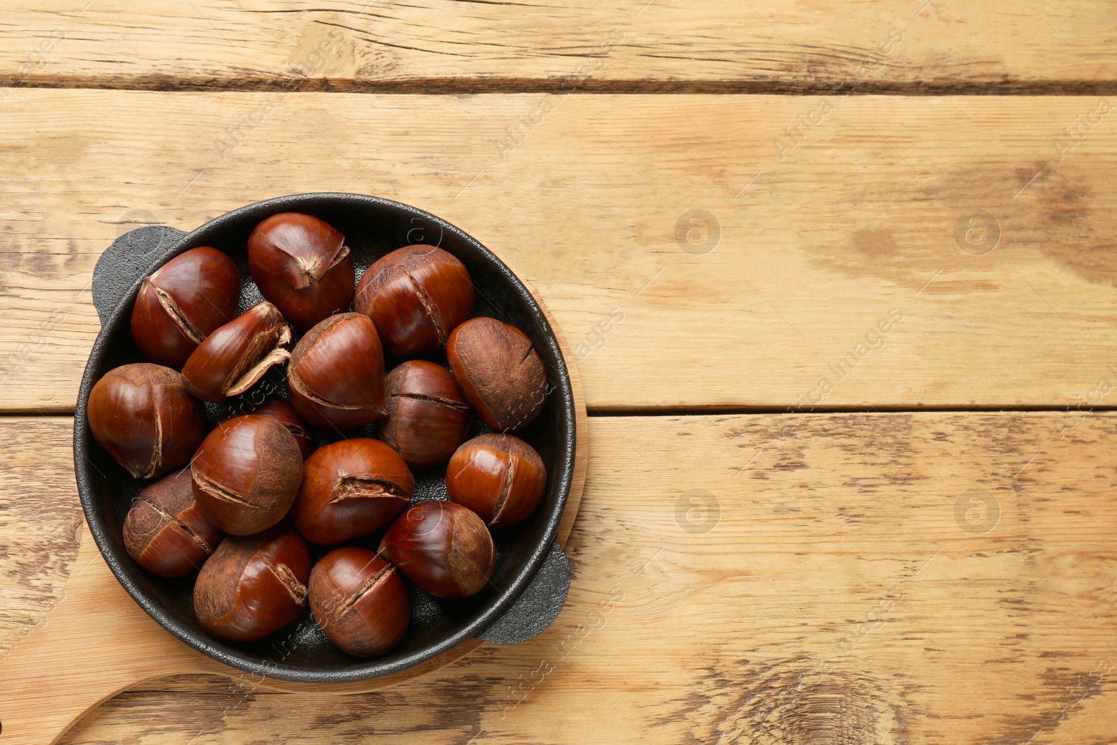 Photo of Fresh edible sweet chestnuts in frying pan on wooden table, top view. Space for text