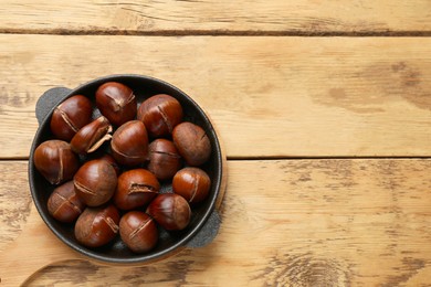Photo of Fresh edible sweet chestnuts in frying pan on wooden table, top view. Space for text