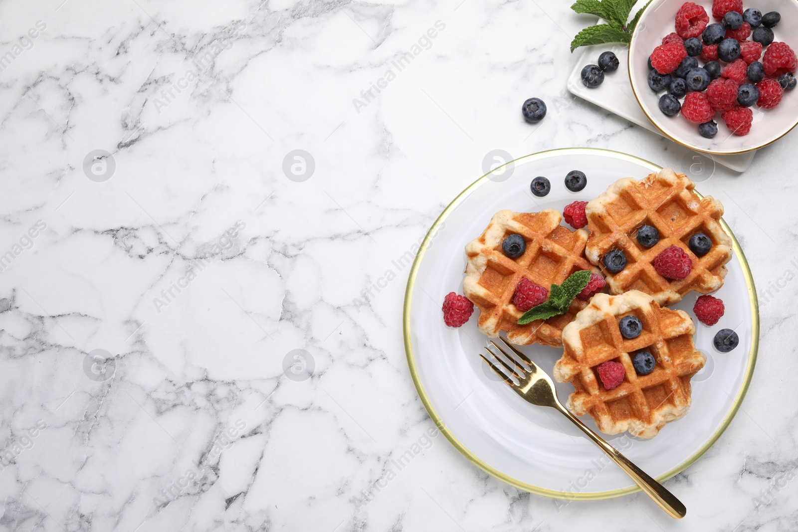 Photo of Delicious Belgian waffles with fresh berries and mint on white marble table, flat lay. Space for text