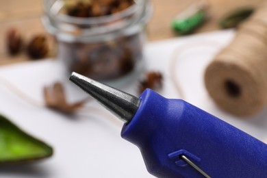 Photo of Hot glue gun over table with handicraft materials, closeup