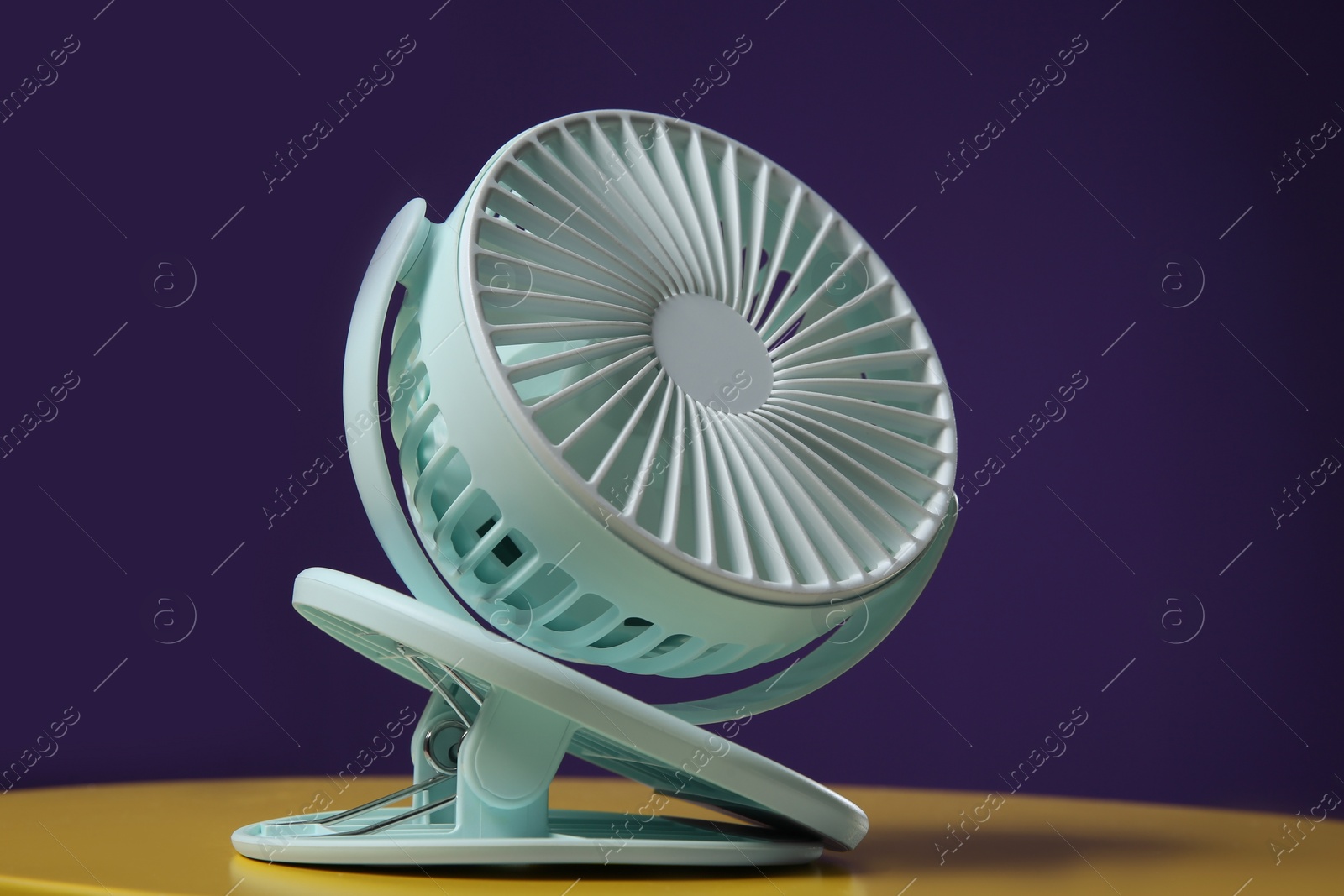 Photo of Modern electric fan on yellow table against violet background