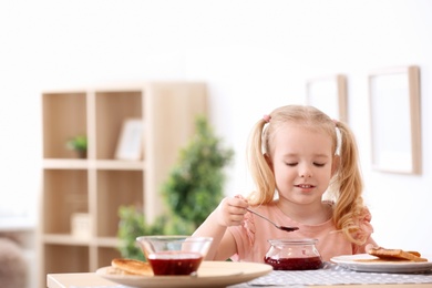 Photo of Cute little girl with jam and tasty toasted bread at table