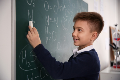 Photo of Schoolboy writing chemical formulas on chalkboard in classroom