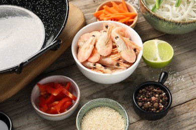 Photo of Different products, spices and black wok on wooden table, closeup