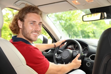 Photo of Attractive young man driving his luxury car, view from backseat
