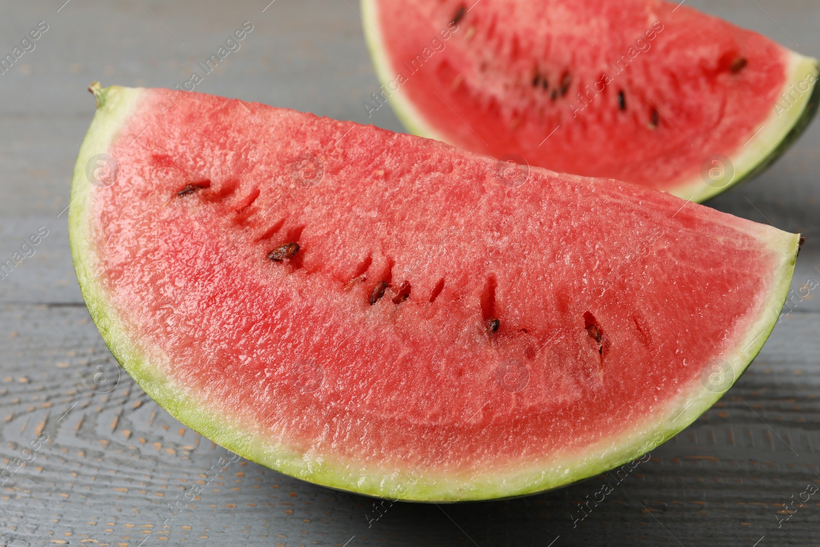 Photo of Slices of tasty ripe watermelon on grey wooden table, closeup