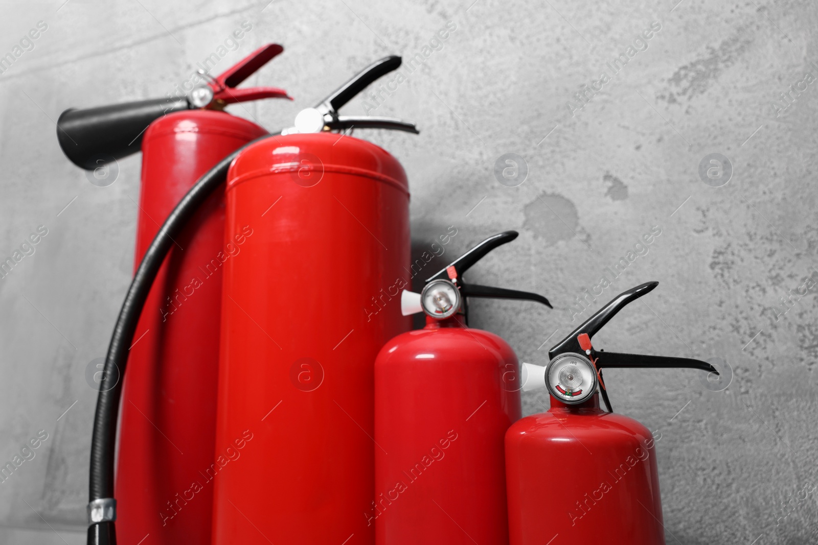 Photo of Four red fire extinguishers near grey wall