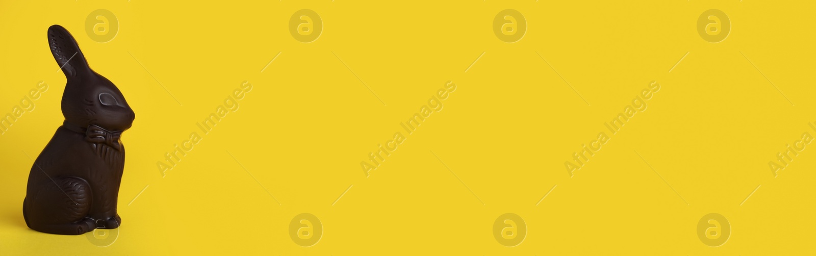 Photo of Dark chocolate bunny on yellow background, space for text. Easter celebration