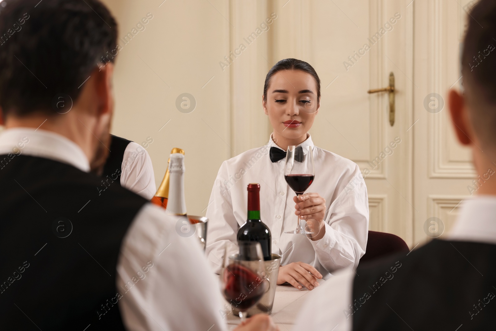 Photo of Group of people tasting red wine in glasses at table indoors. Professional butler courses