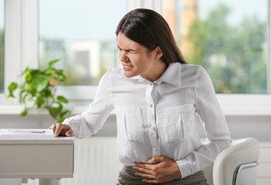 Photo of Young woman suffering from menstrual pain in office