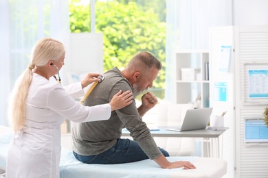 Photo of Doctor examining coughing mature man at clinic