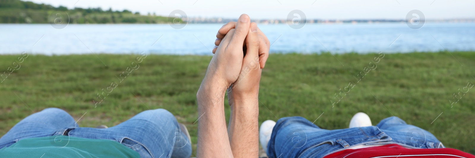 Image of Gay couple lying near river on sunny day, closeup. Banner design