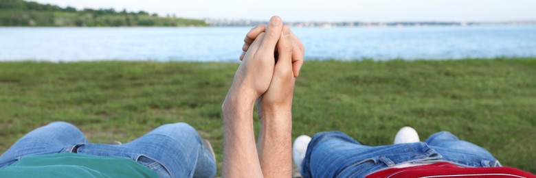 Gay couple lying near river on sunny day, closeup. Banner design