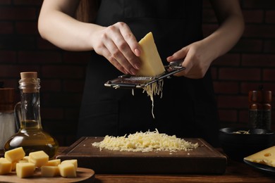 Photo of Woman grating cheese at wooden table, closeup
