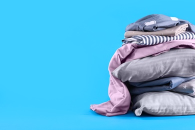 Photo of Stack of clean bed sheets and pillows on blue background. Space for text