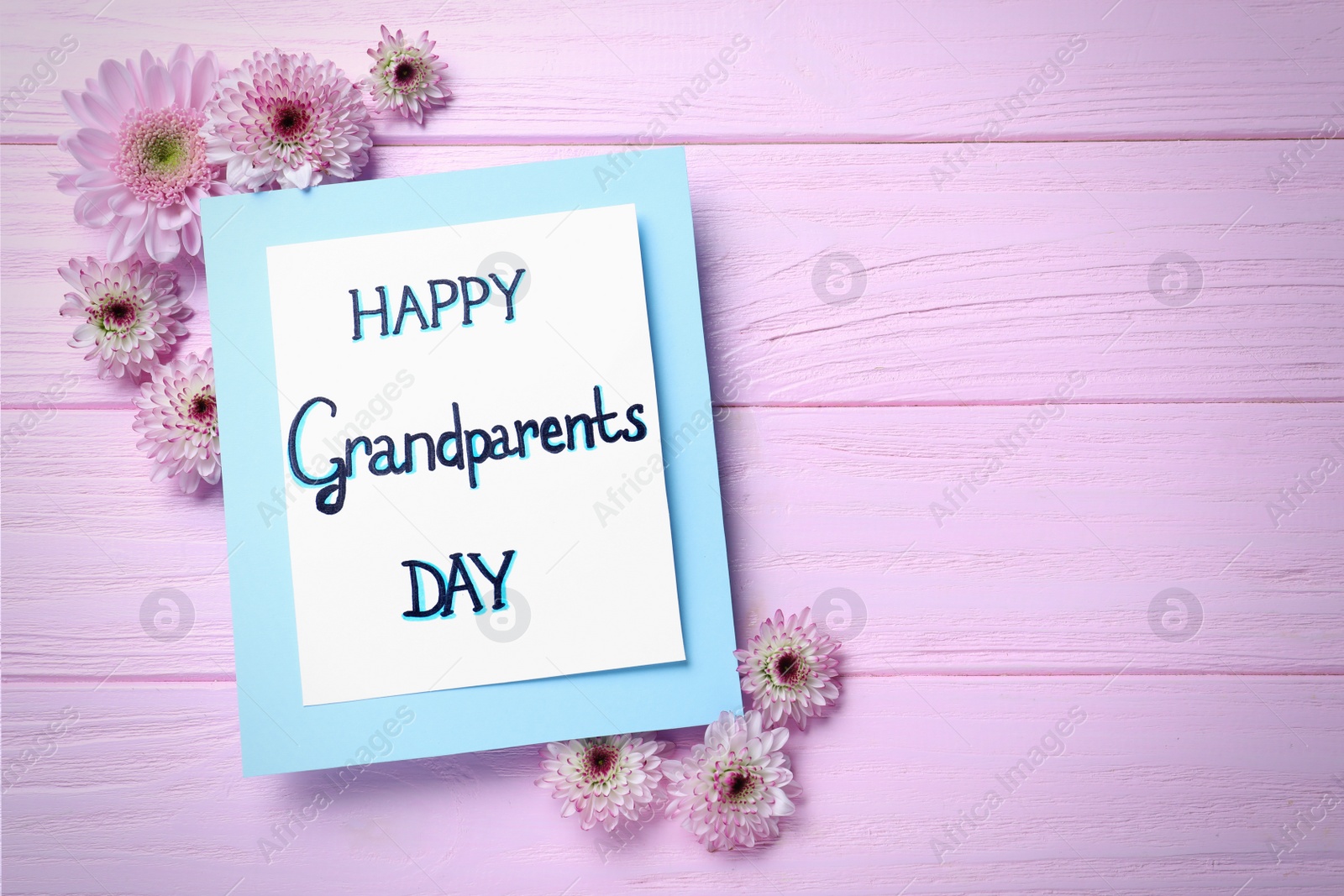 Photo of Beautiful flowers and card with phrase Happy Grandparents Day on pink wooden table, flat lay. Space for text