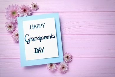 Photo of Beautiful flowers and card with phrase Happy Grandparents Day on pink wooden table, flat lay. Space for text