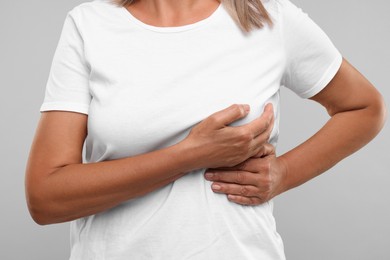 Photo of Woman doing breast self-examination on light grey background, closeup