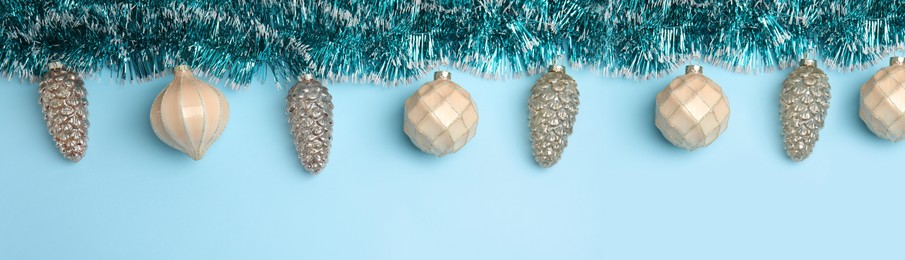 Image of Shiny tinsel and Christmas balls on light blue background, flat lay. Banner design