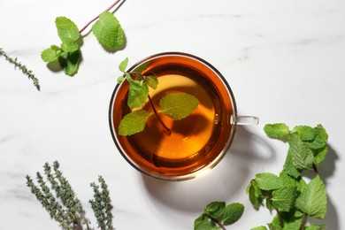 Photo of Cup of aromatic herbal tea with mint and thyme on white marble table, flat lay