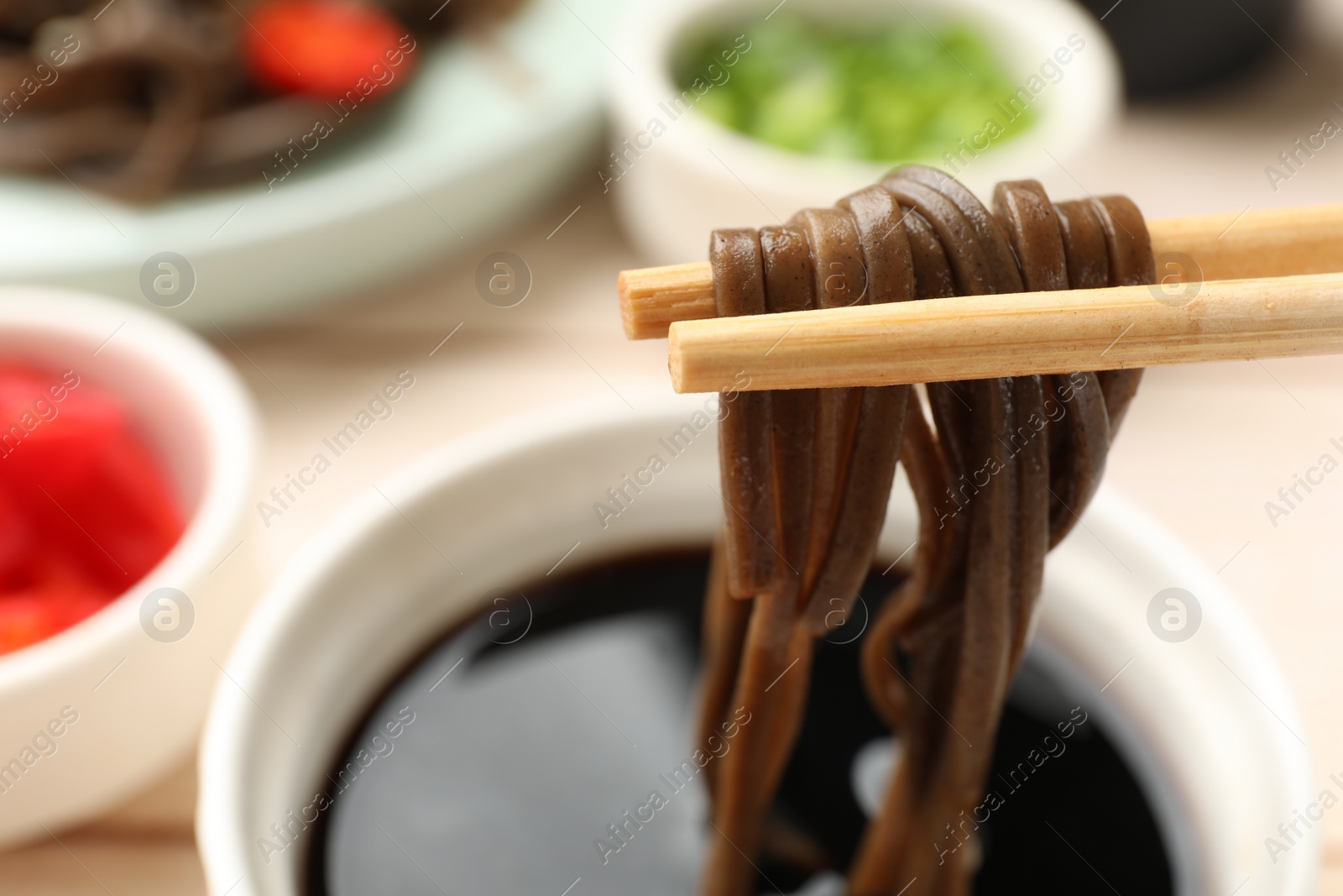 Photo of Eating delicious buckwheat noodles (soba) with chopsticks at table, closeup. Space for text