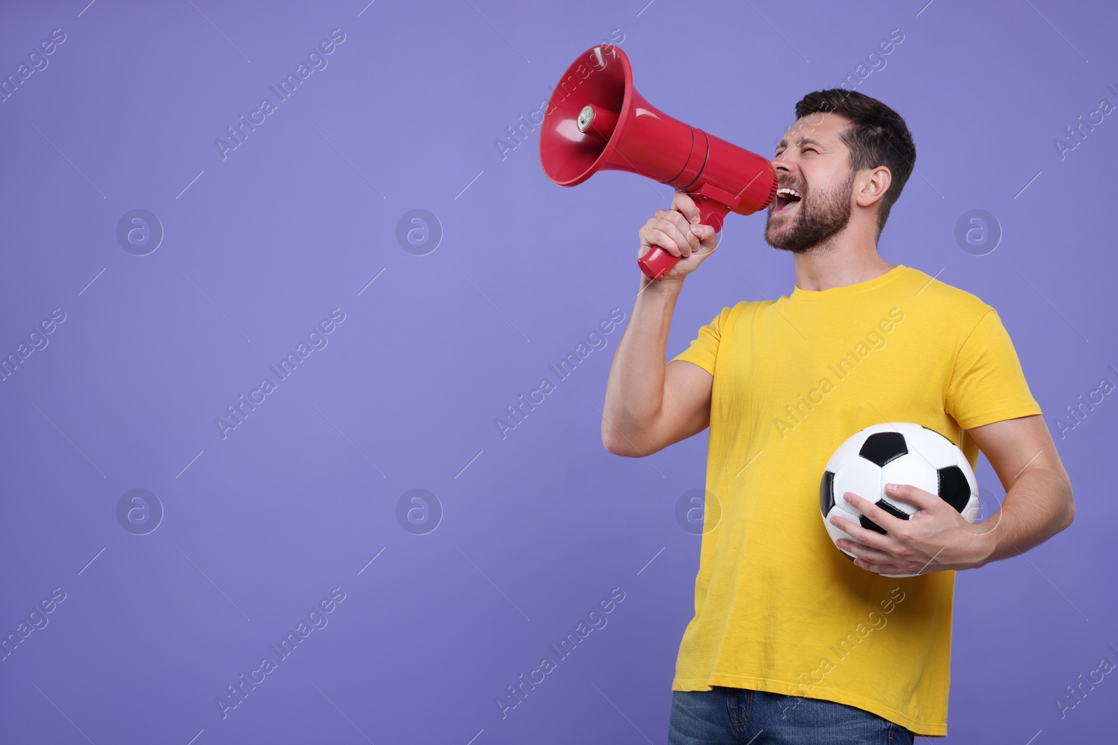 Photo of Emotional sports fan with ball and megaphone on purple background. Space for text