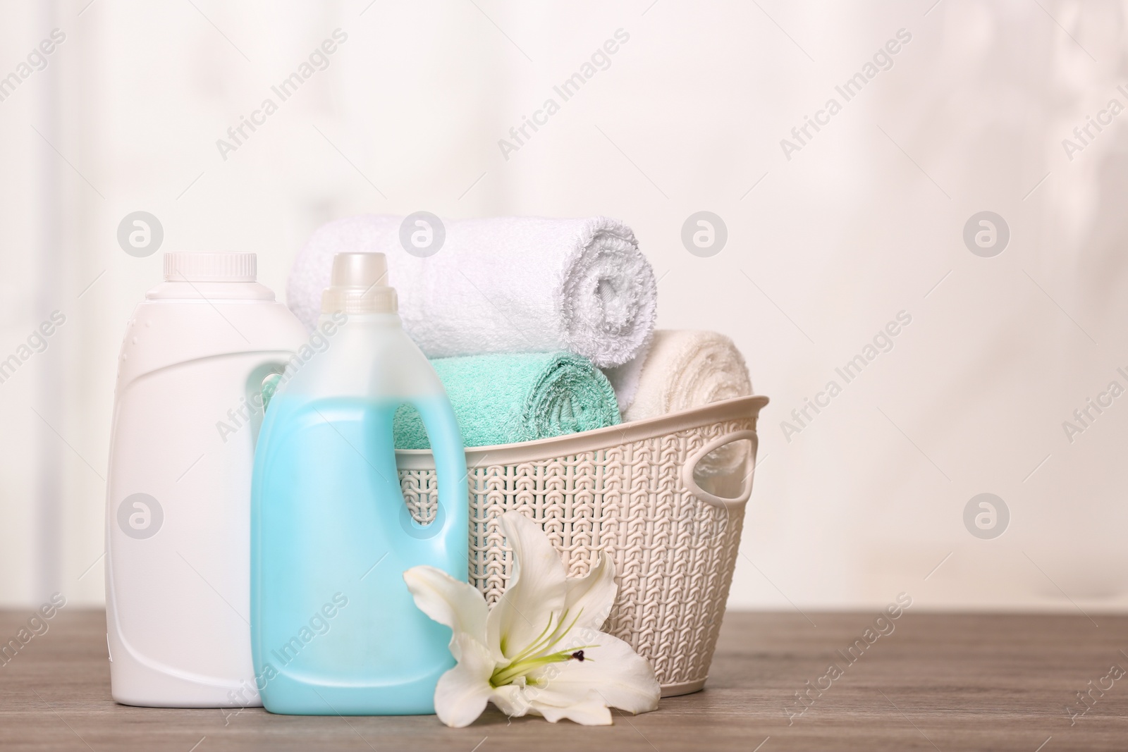 Photo of Clean towels in basket with lily and detergents on table. Space for text
