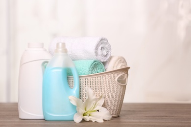 Clean towels in basket with lily and detergents on table. Space for text