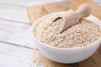 Photo of Raw barley groats and scoop in bowl on white wooden table, closeup. Space for text