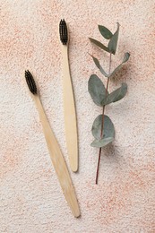 Photo of Bamboo toothbrushes and eucalyptus branch on beige textured table, flat lay