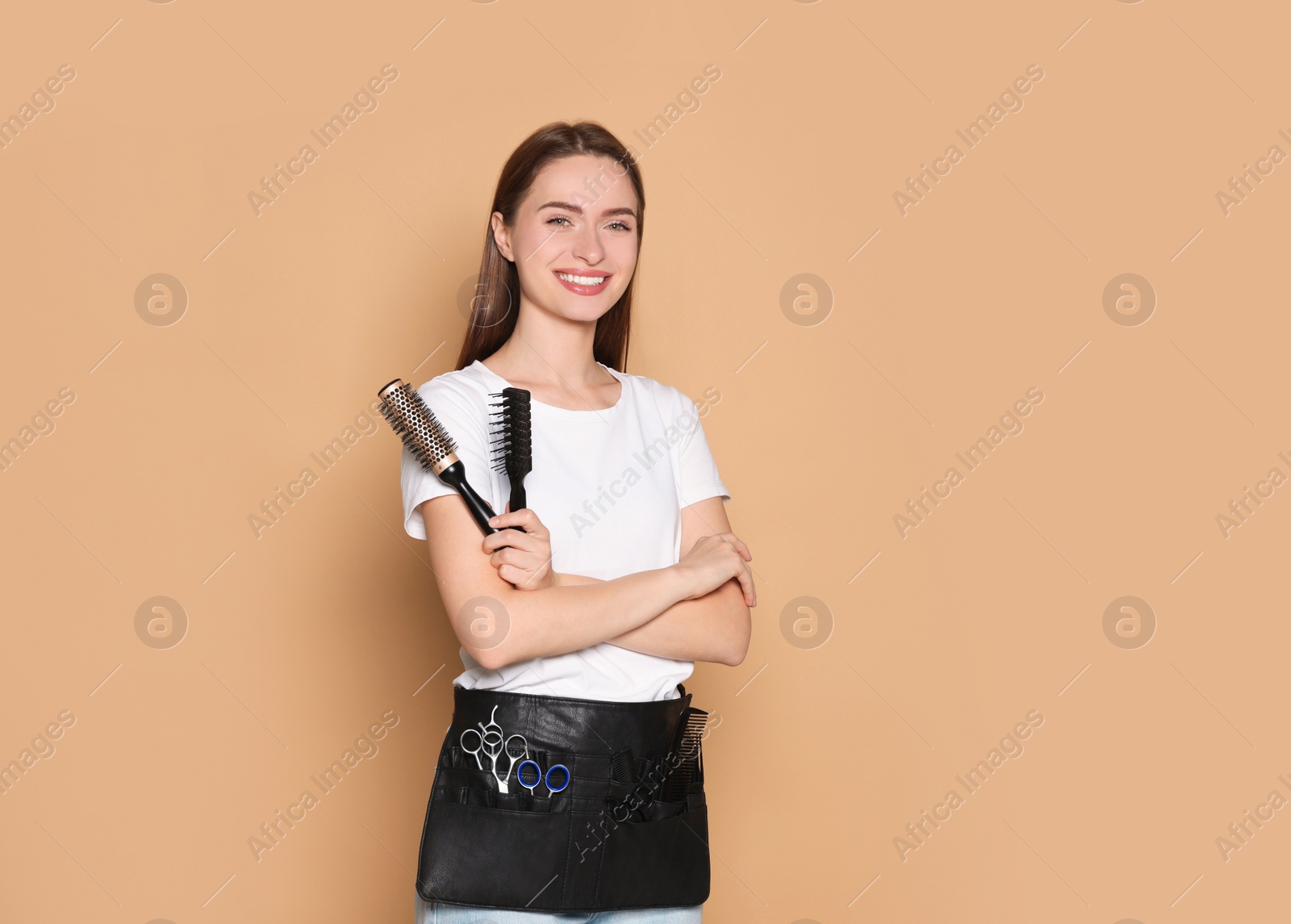 Photo of Portrait of happy hairdresser with brushes on beige background. Space for text