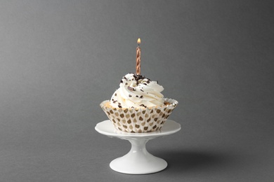 Delicious birthday cupcake with candle on grey background