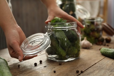 Photo of Woman pickling glass jar of cucumbers at wooden kitchen table, closeup